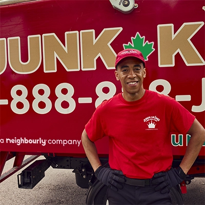 Junk King professional standing by a red branded truck with hands on his hips.
