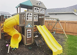 A wooden swingset with bright yellow slides.
