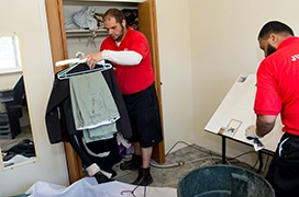 Two Junk King professionals removing clothing from a closet.