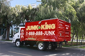 Red Junk King dump truck parked on a street in front of greenery.