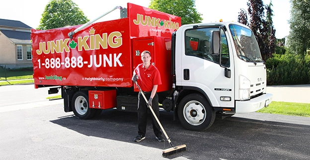 A Junk King professional using a push broom beside a branded dump truck.