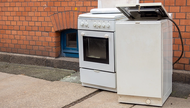 Old appliances sitting outside of a brick building.