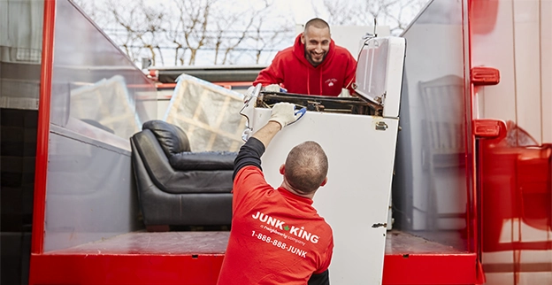 Two Junk King professionals loading a washing machine onto a truck bed.