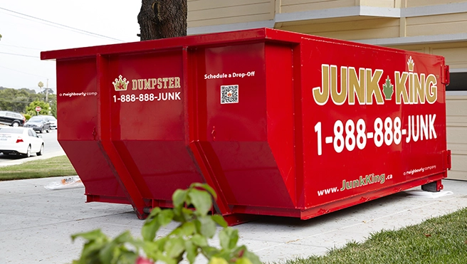 A red dumpster outside of a garage.