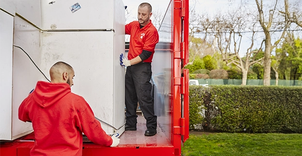 Junk King professionals unloading a refrigerator from the back of a truck.