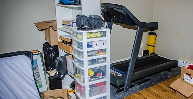 A room in a home with a treadmill and storage containers.