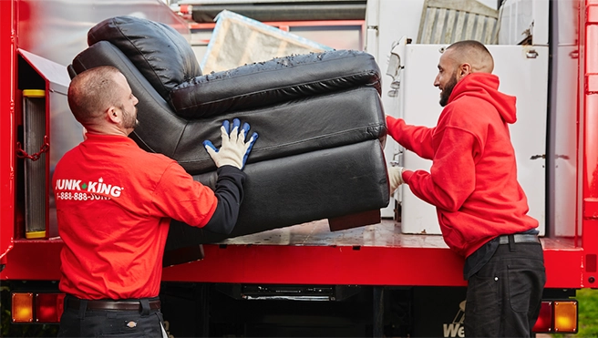 Junk King professionals loading a recliner into the back of a truck.