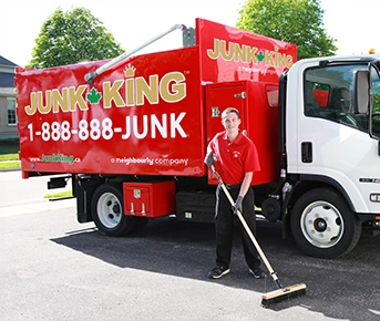 Junk King professional standing beside a dump truck with a push broom.