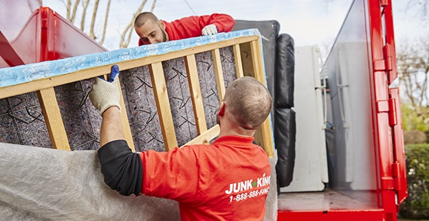 Two Junk King professionals loading a mattress onto a truck.