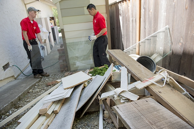 A pile of miscellaneous junk outside of a home with two Junk King professionals standing nearby.