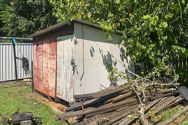 An old metal shed with a pile of wood next to it.