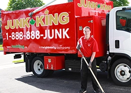 Red Junk King dump truck with an employee using a push broom beside it.